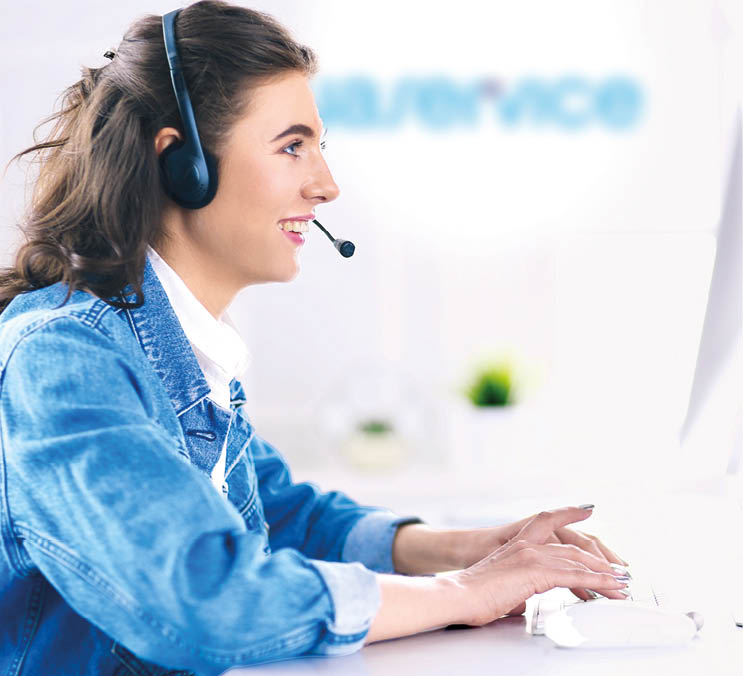 Happy charming young woman sitting and working with laptop using headset in office.