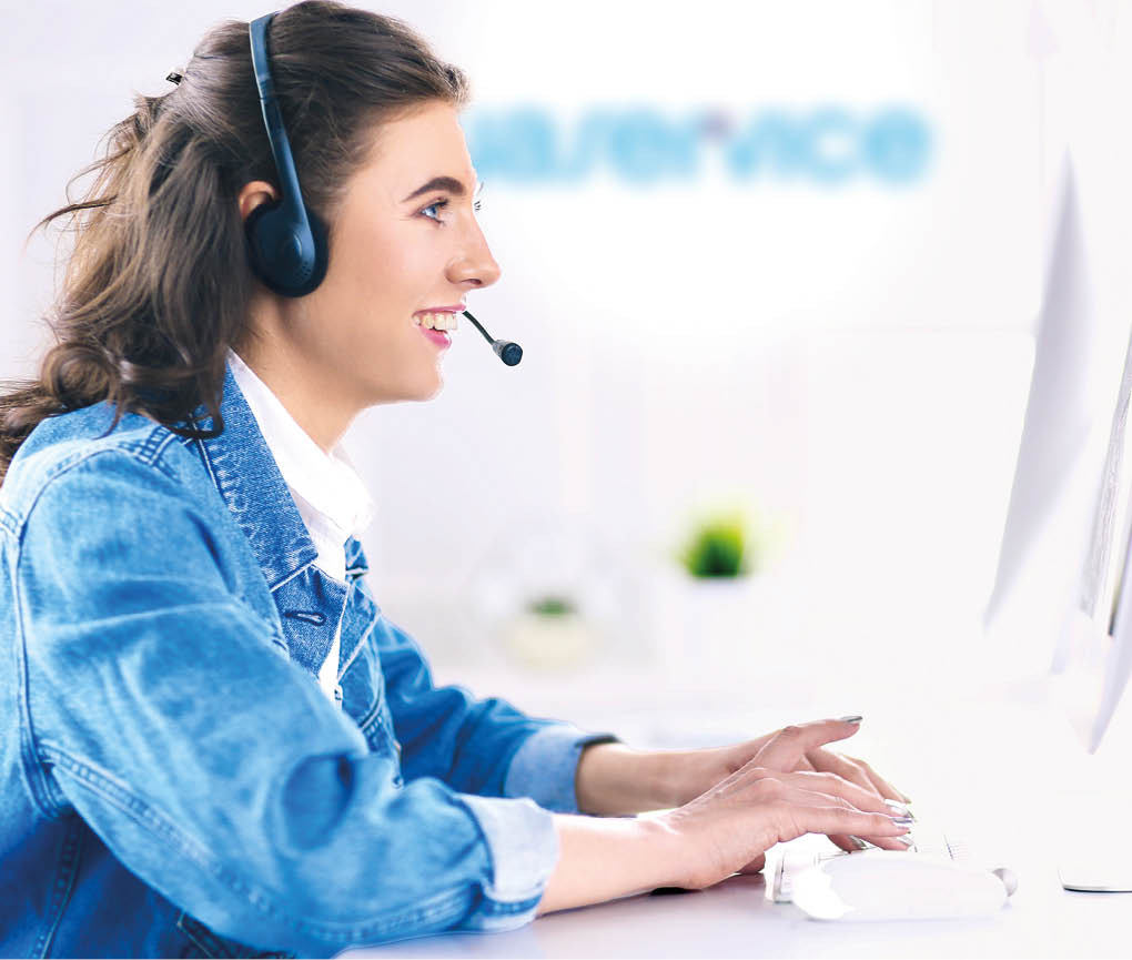 Happy charming young woman sitting and working with laptop using headset in office.